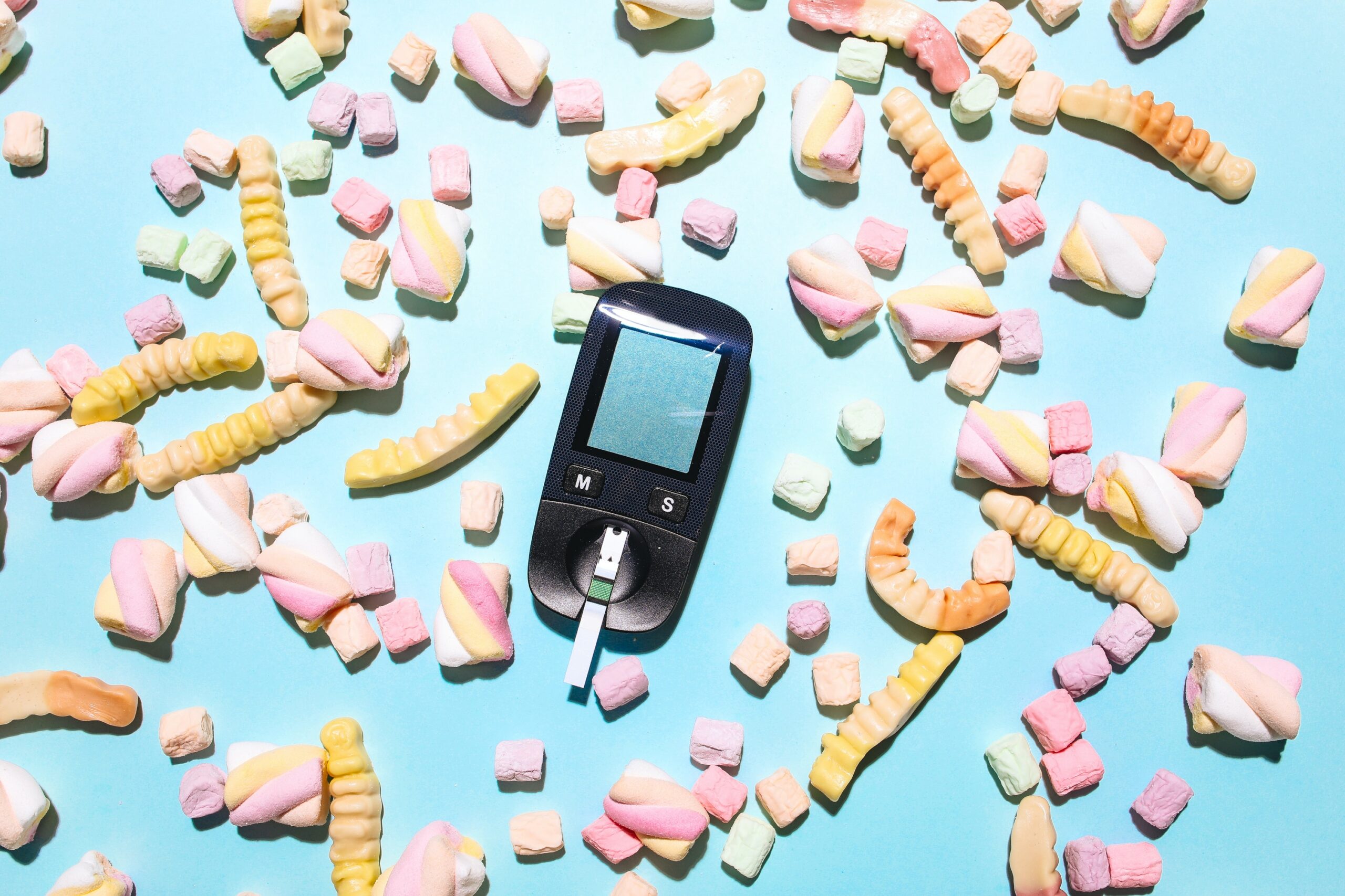 Glucose meter surrounded by sweets on a blue surface