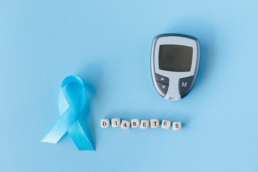 A glucose meter, a blue ribbon, and dice saying diabetes.