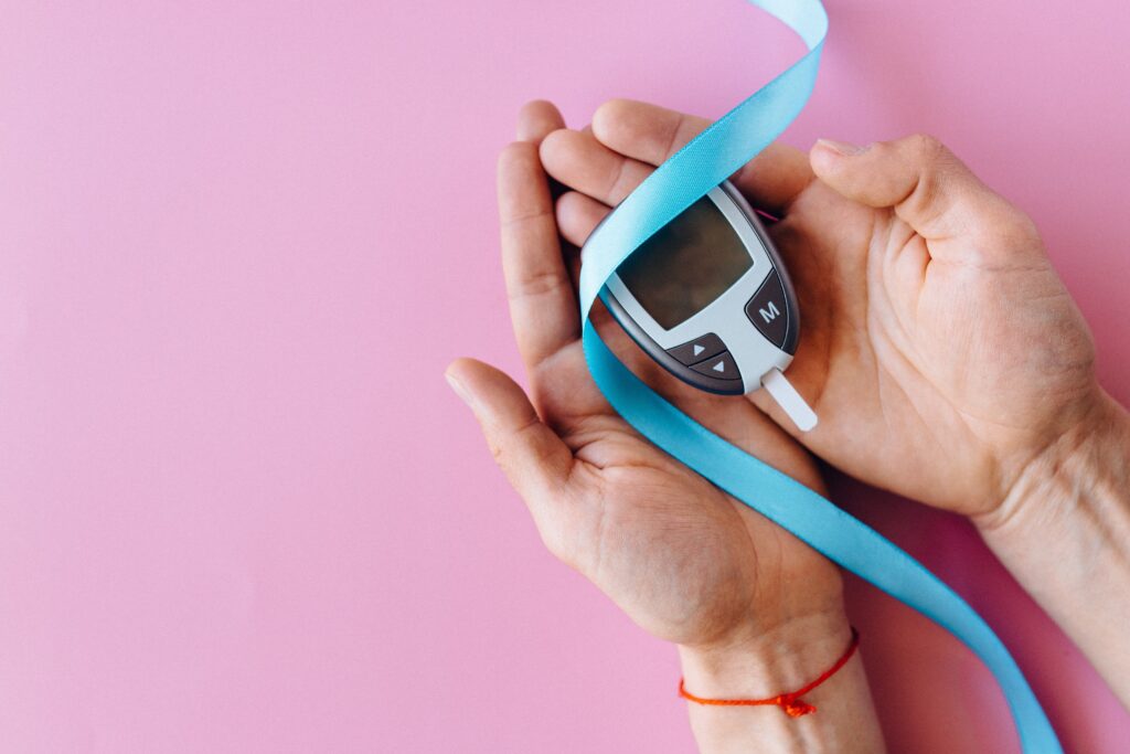 A view of a person's hands holding a glucose meter and a thin blue ribbon.