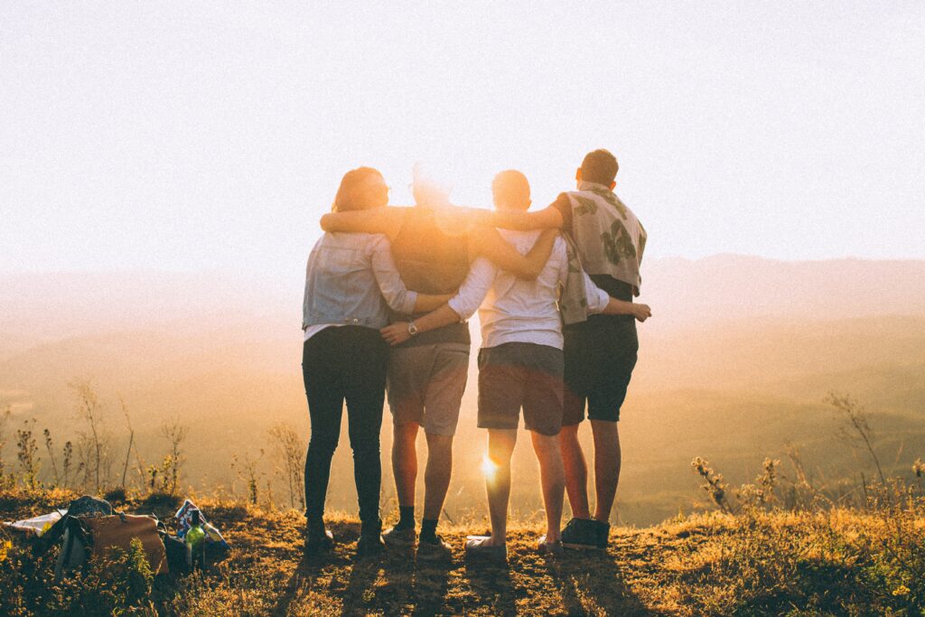 A group of 4 people standing near a cliff looking at the sunset.