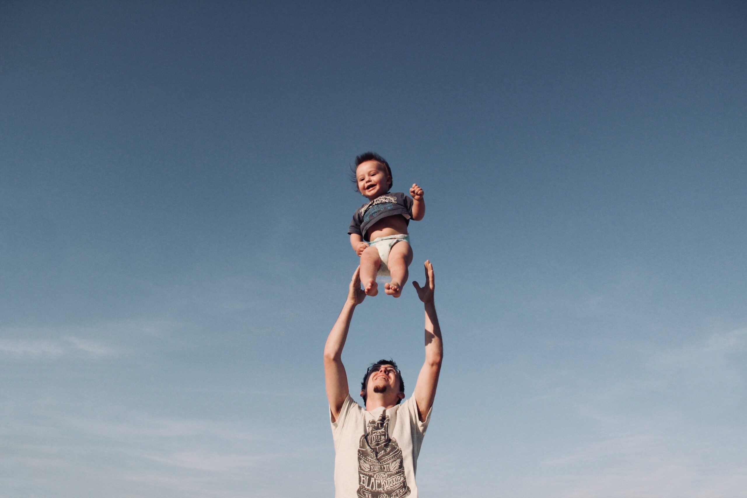 A father throwing his toddler into the air while the child is smiling.