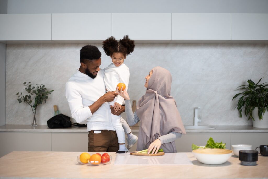 A mother, father, and child cutting up fruits and vegetables in the kitchen.