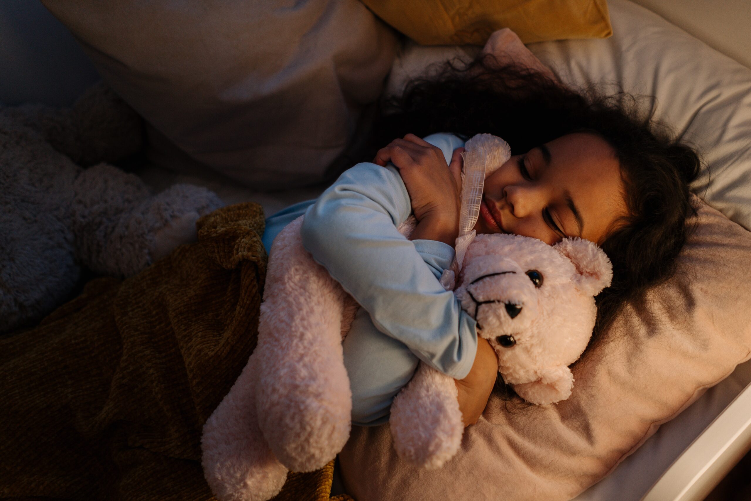A girl asleep hugging a teddy bear.