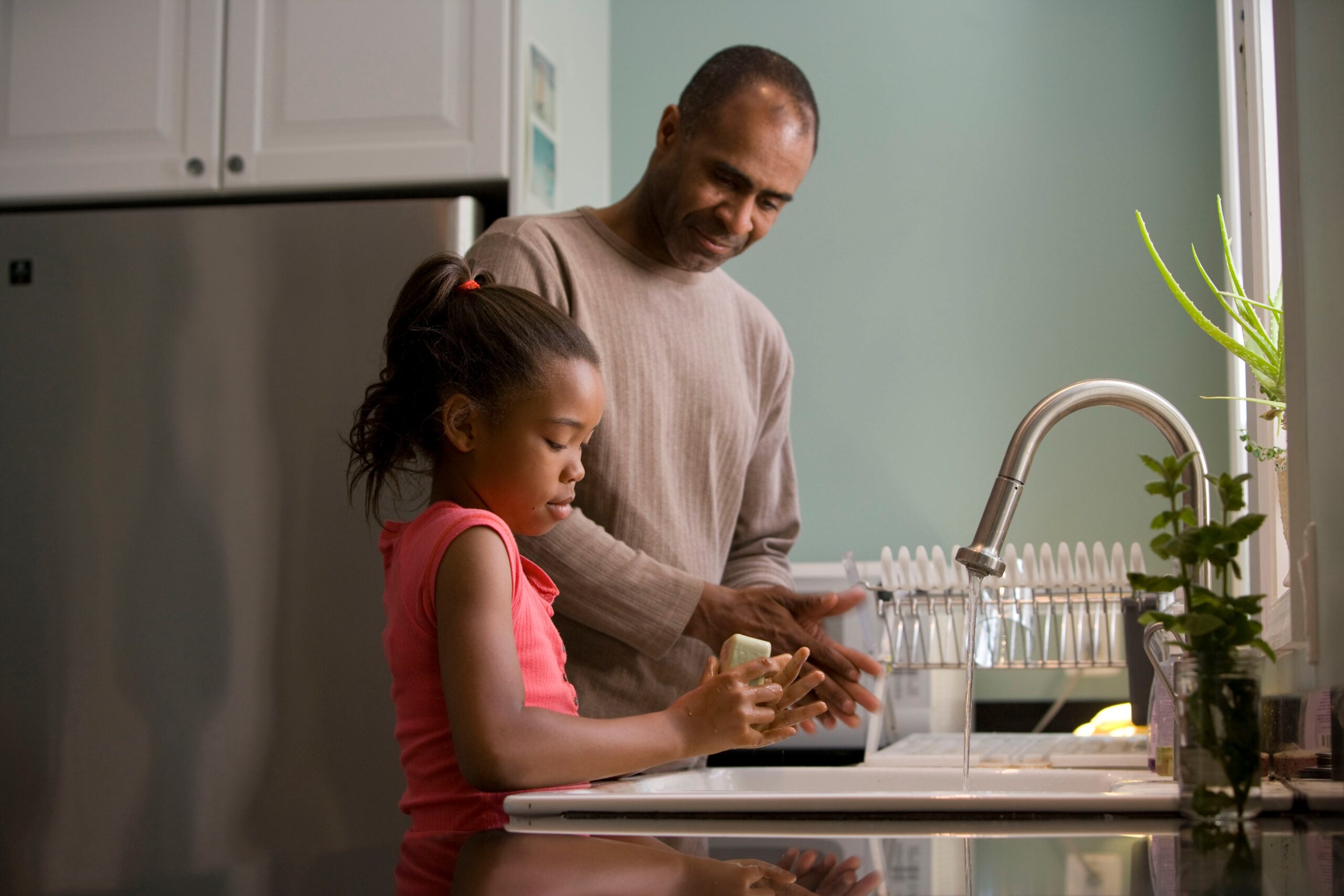 Father teaching daughter to wash hands in the kitchen.