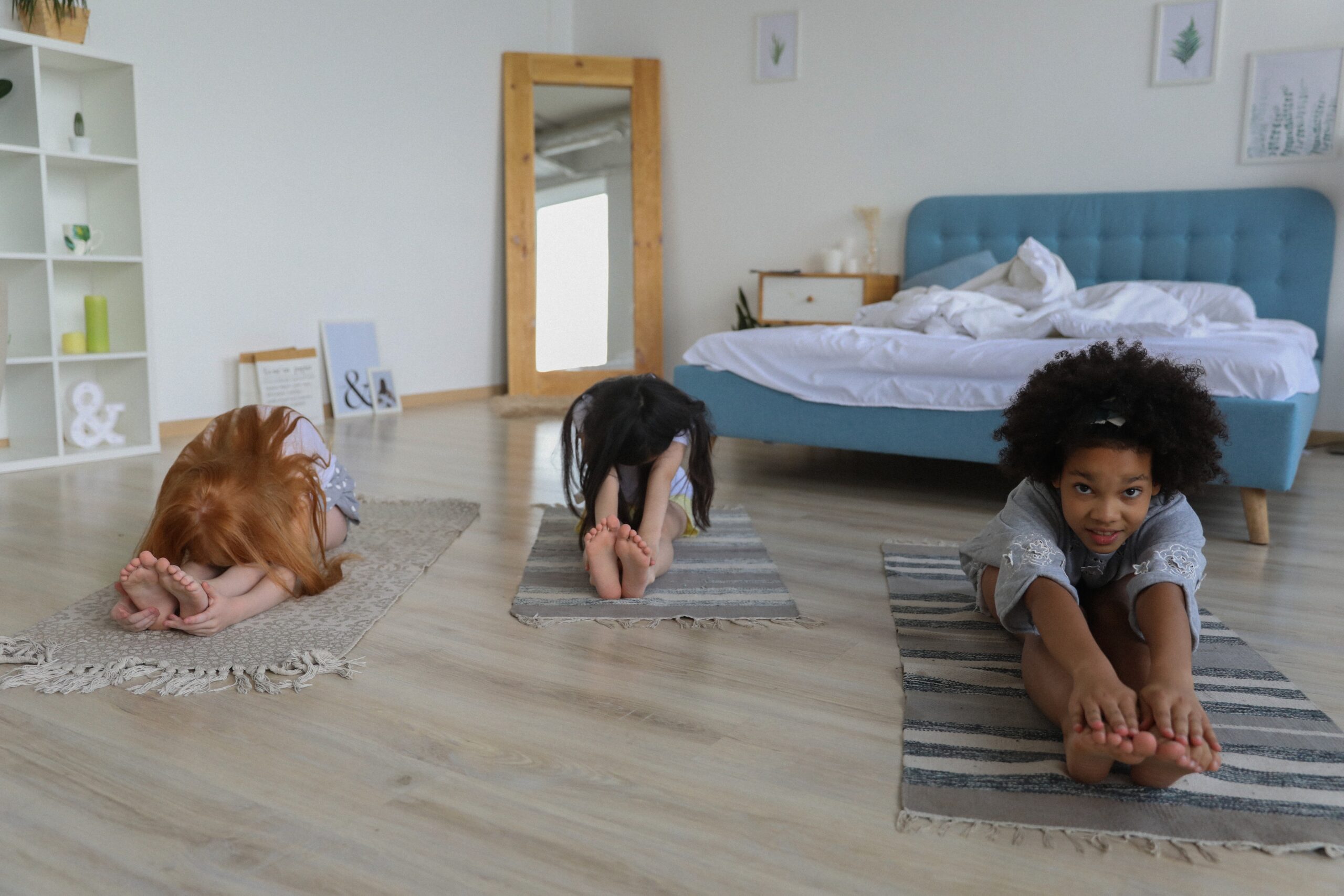 Three girls stretching on a floor in a bedroom.
