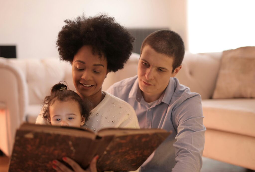 Parents and child reading a large book together, fostering a love for reading.