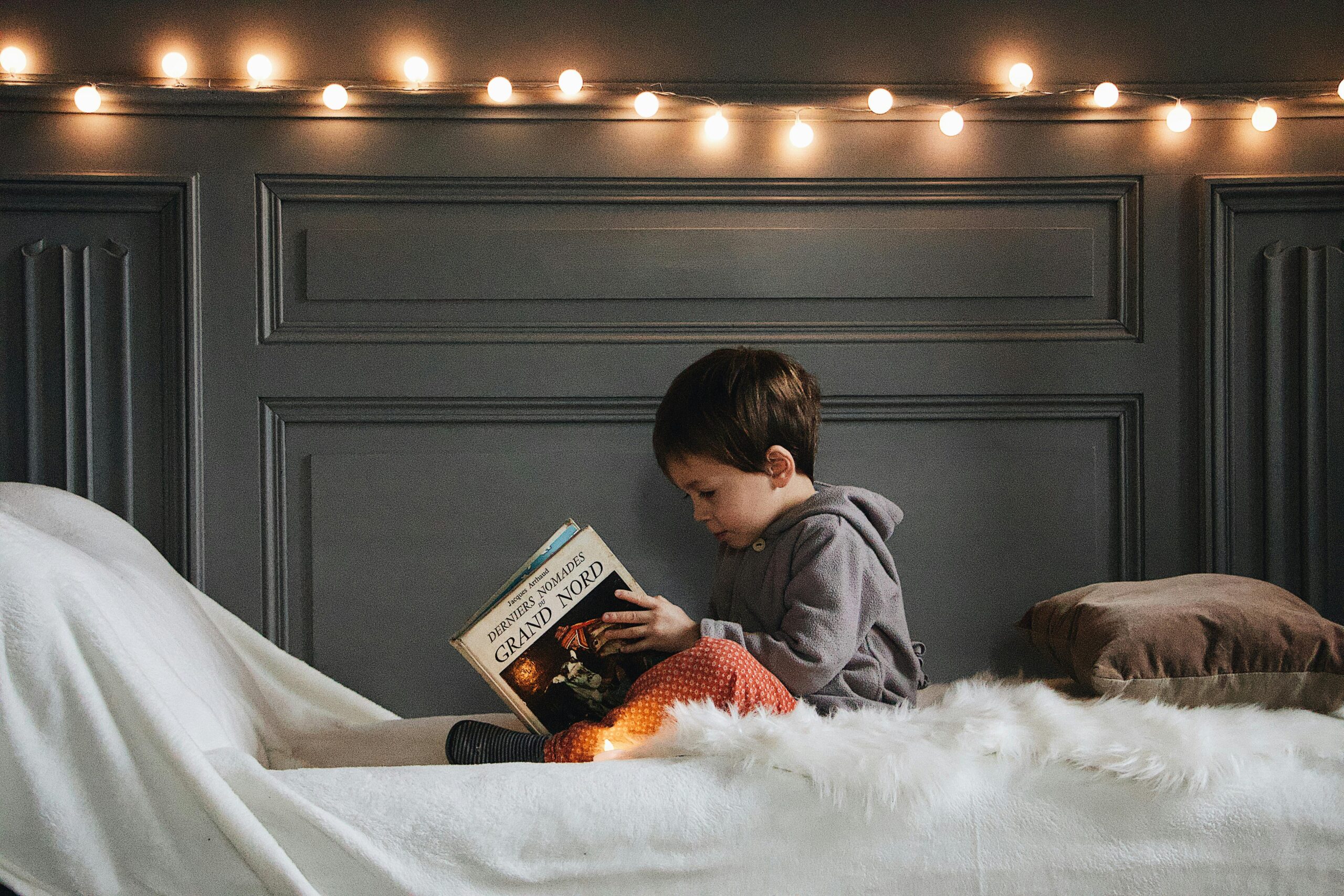 A child reading a book on a bed with fairy lights in the background, creating a cozy atmosphere.